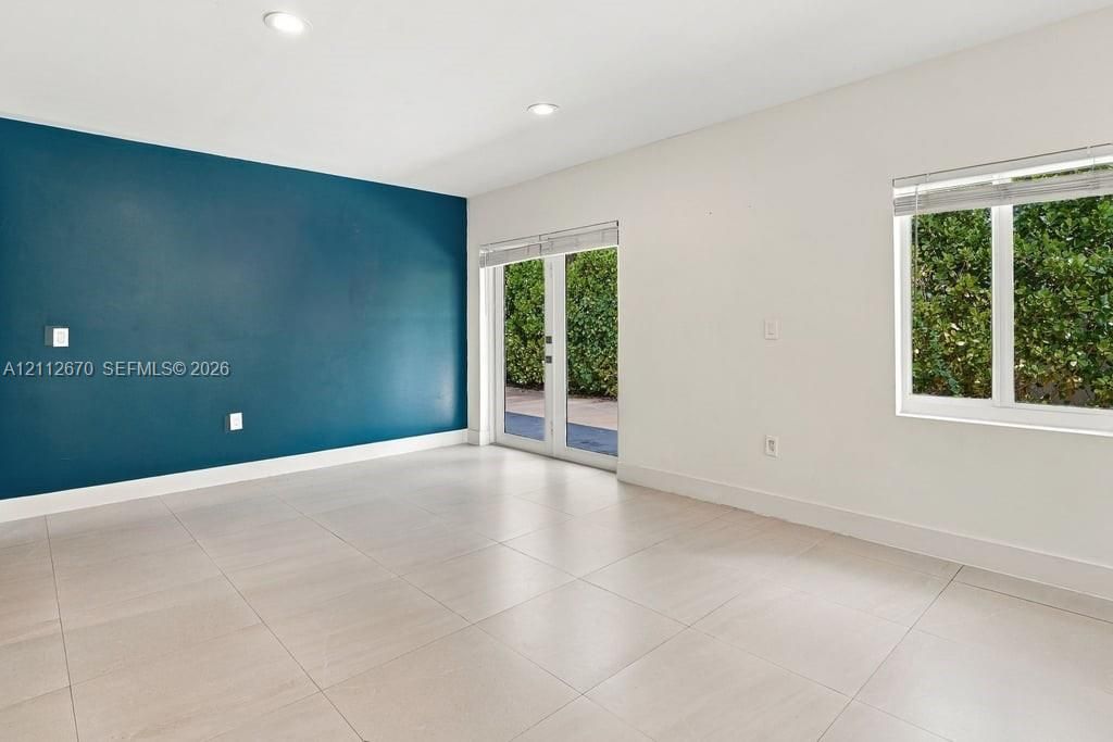 Interior space featuring large-format tile flooring, a bold teal accent wall, recessed lighting, double glass-panel doors, and white-framed windows