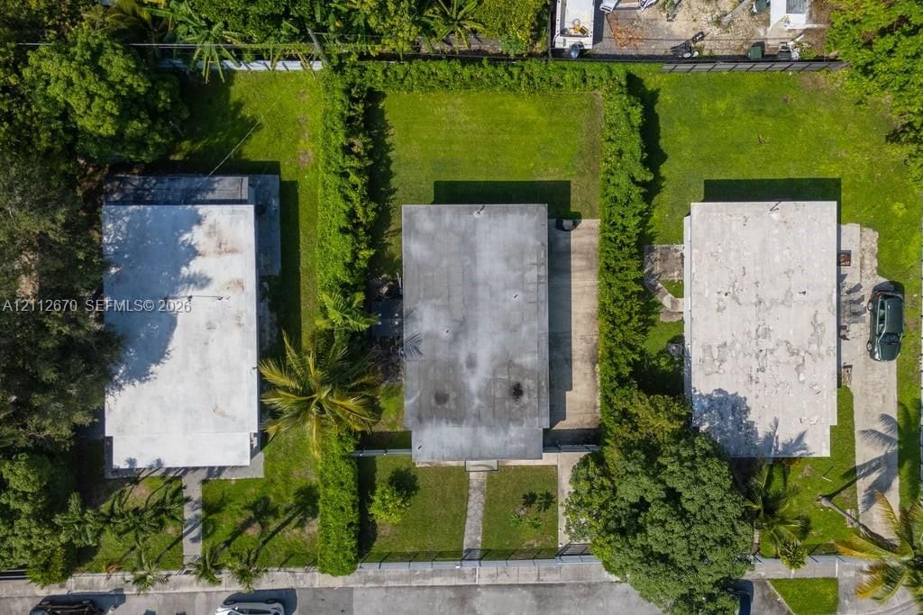 Aerial perspective featuring a rectangular lot, mature perimeter landscaping, concrete driveway, and established lawn