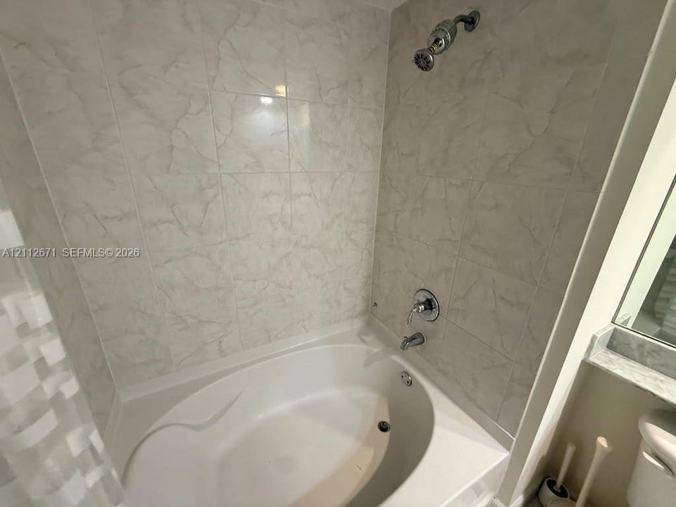 Oval soaking tub featuring light-toned tile surround, polished metal shower fixtures, and integrated ledge shelving