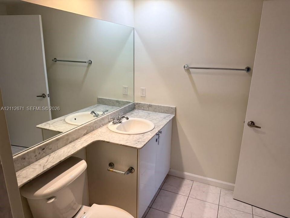 Vanity with integrated sink, stone-finish countertop, full-width mirror, and ceramic tile flooring