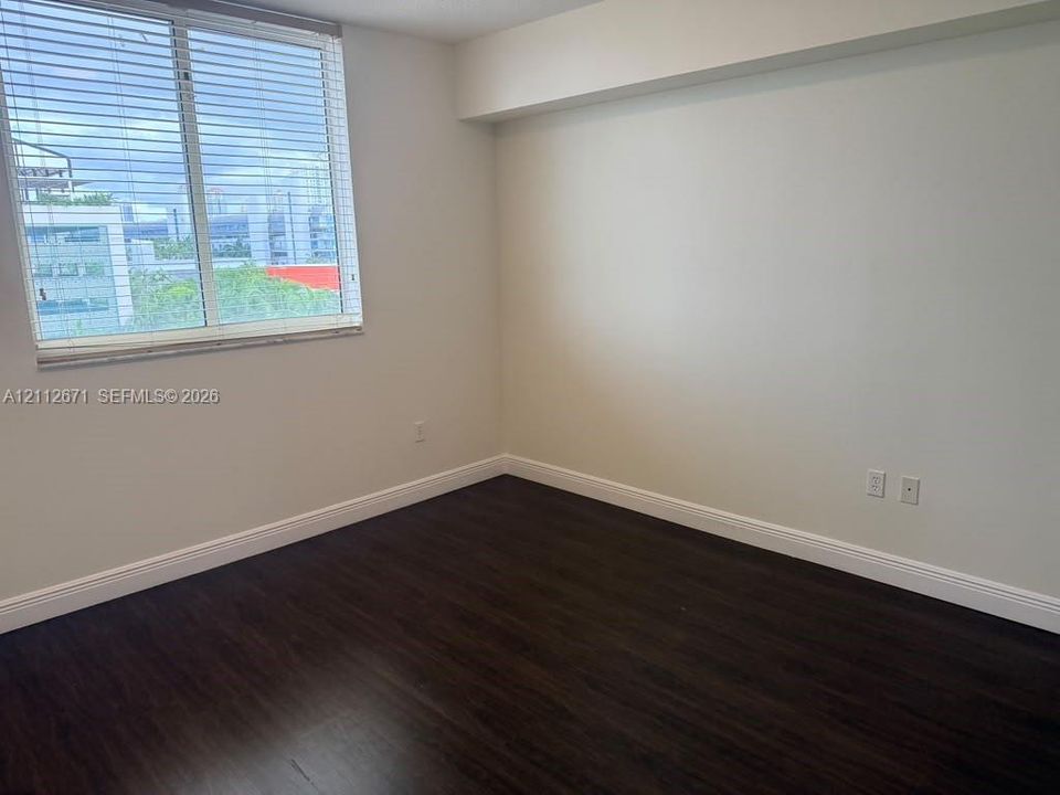 Neutral interior featuring dark wood-finish flooring, a large window with horizontal blinds, and smooth, light-toned walls