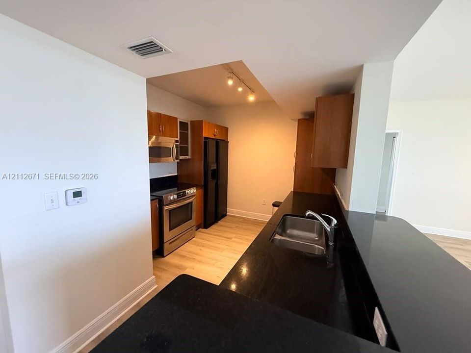 Kitchen featuring dark stone countertops, wood-finish cabinetry, stainless steel appliances, and track lighting