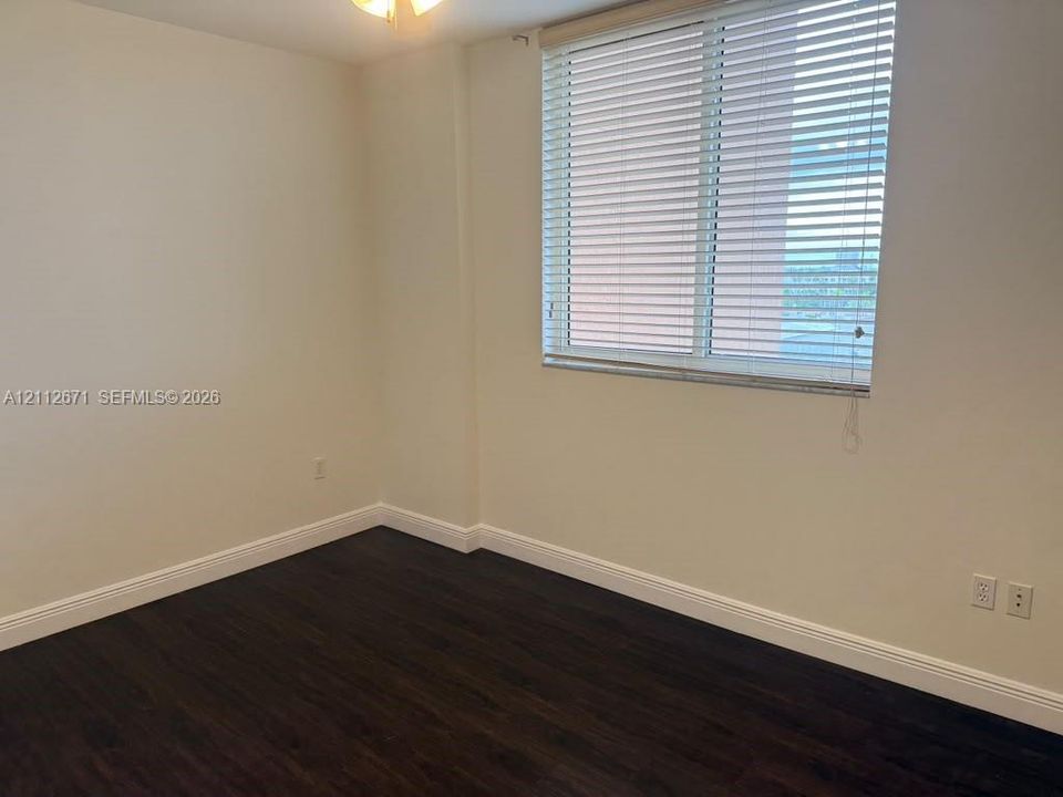 Room featuring wood-finish flooring, neutral walls, and a large window equipped with horizontal blinds
