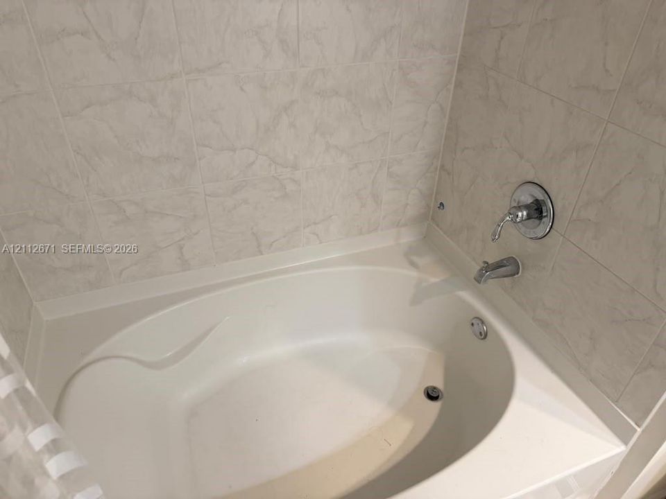 Oval soaking tub featuring light-toned textured tile surround and chrome plumbing fixtures