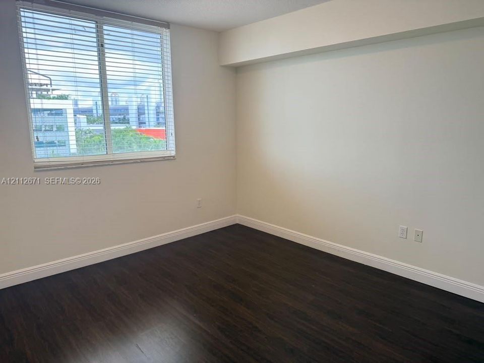 Neutral interior with dark wood-finish flooring, white walls, and a window with horizontal blinds