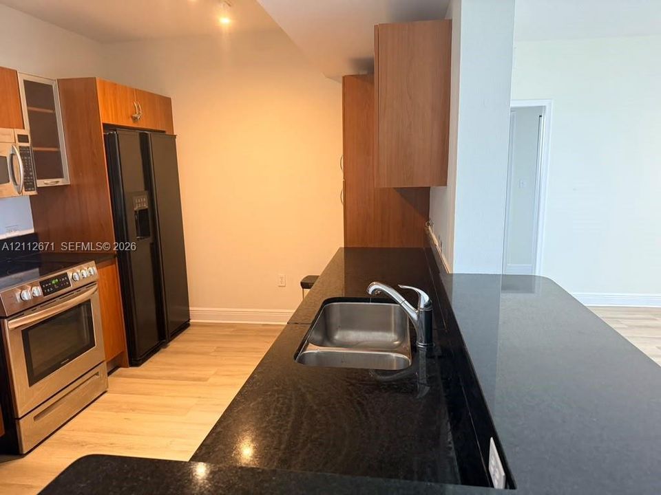 Kitchen featuring wood-finish cabinetry, dark stone countertops, stainless steel appliances, and dual-basin stainless steel sink with high-arc faucet