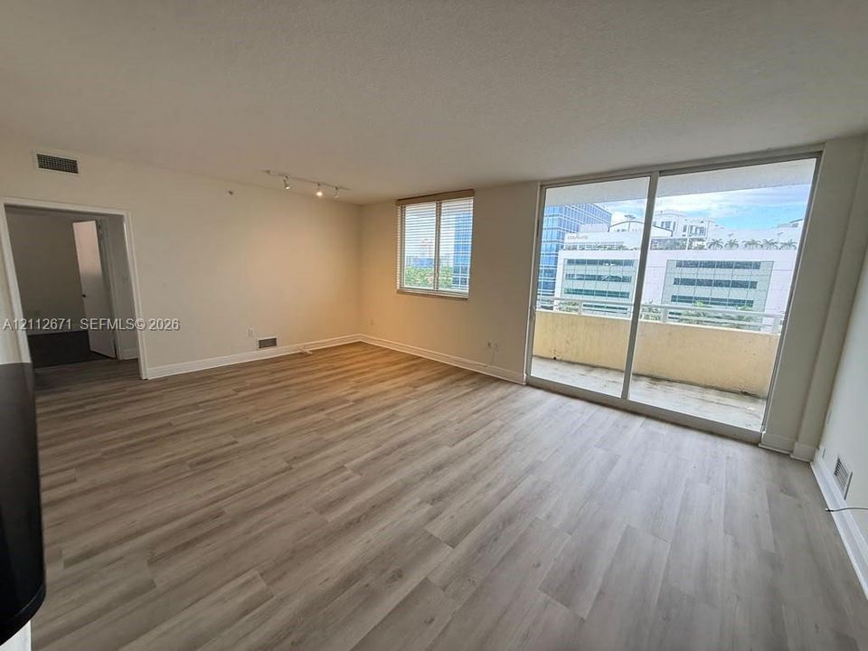 Living area featuring wood-finish flooring, sliding glass doors to a private balcony, multi-directional track lighting, and neutral-toned walls