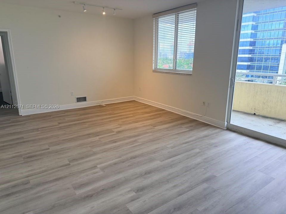 Open-concept room featuring wood-finish flooring, a glass sliding door to a balcony, track lighting, and a window with horizontal blinds