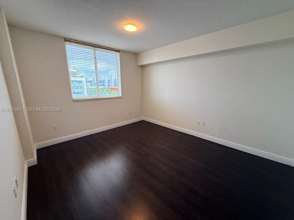 Room featuring dark wood-finish flooring, neutral wall tones, a window with horizontal blinds, and a flush-mount ceiling light fixture