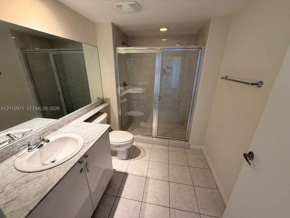 Bathroom featuring a vanity with a stone-top counter, recessed sink, glass-enclosed shower, large wall-mounted mirror, and ceramic tile flooring