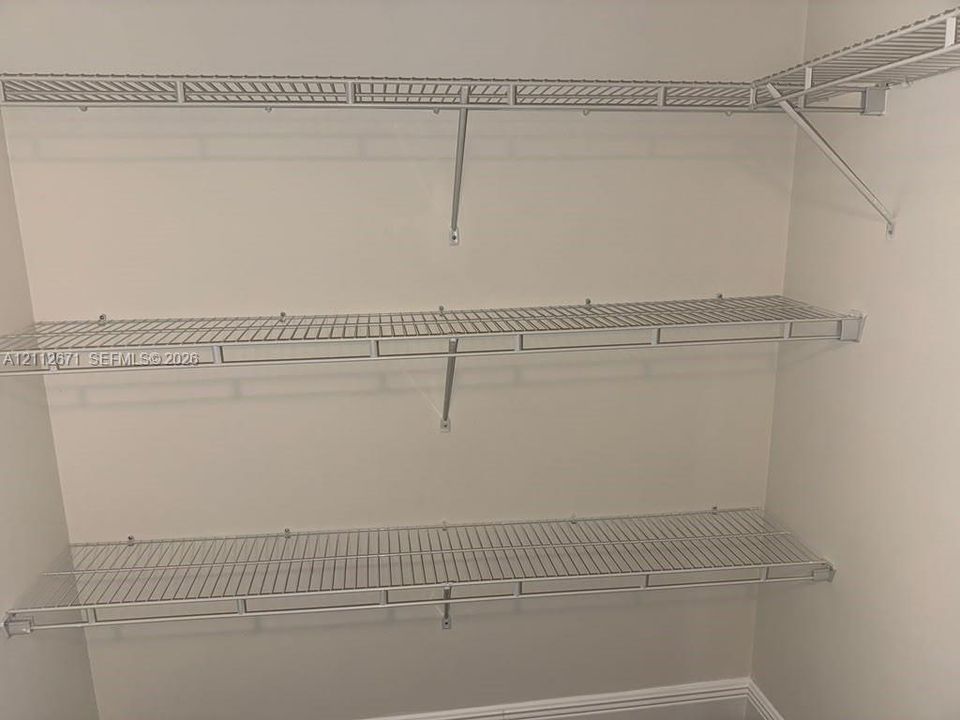 Wall-mounted white wire shelving system featuring three tiered levels of storage