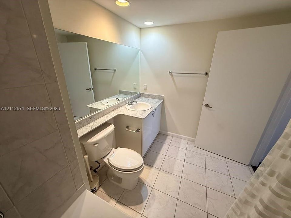 Vanity featuring a stone-patterned countertop and undermount sink, complemented by a full-width wall mirror, tile flooring, and recessed ceiling lighting