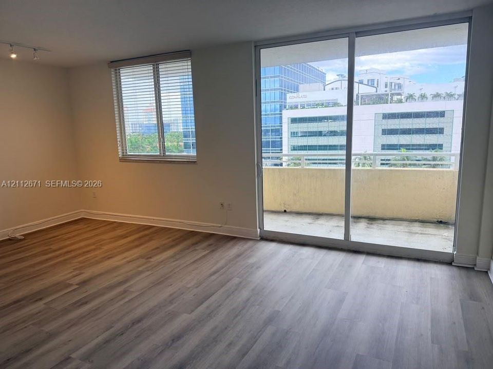 Wood-finish flooring, sliding glass door, private balcony, and multi-pane window with blinds