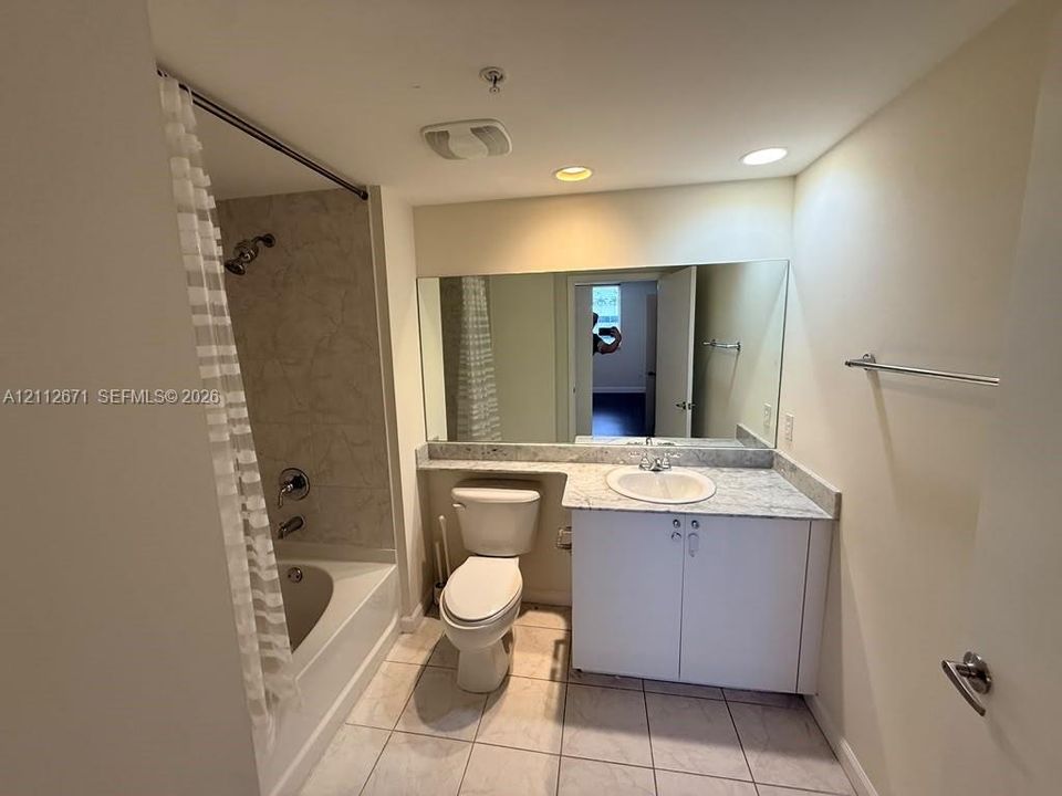 Full-width wall mirror, vanity with stone-surface countertop, integrated basin, tile flooring, and tub-shower combination with tiled surround