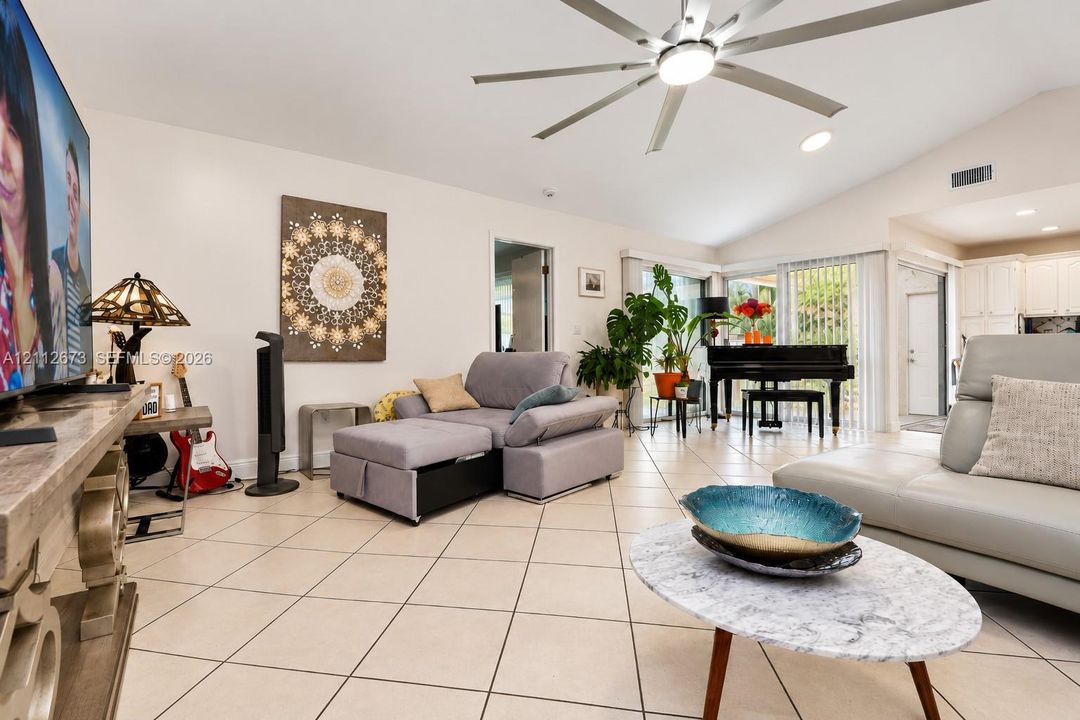 Living area featuring ceramic tile flooring, vaulted ceilings, and a large multi-blade ceiling fan with integrated lighting