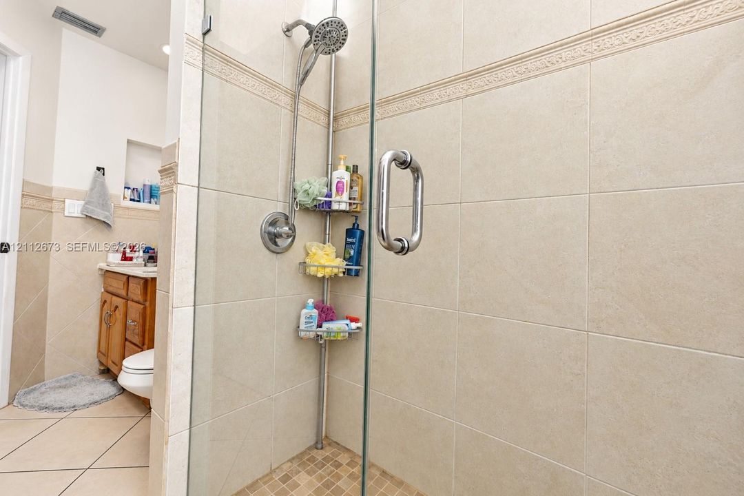 Walk-in shower featuring glass enclosure, large-format neutral wall tile, decorative tile accent band, and built-in wall niche