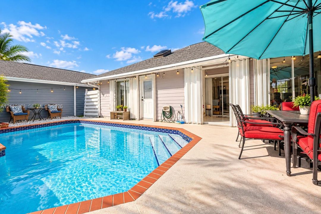 Outdoor living area featuring a swimming pool with tile trim, concrete patio surfacing, horizontal lap siding, and attached string lighting