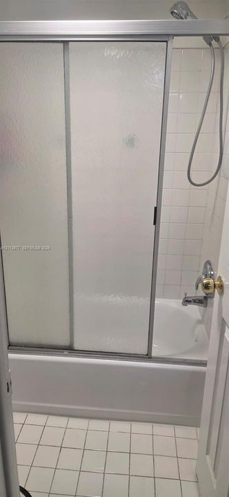 Bathtub and shower combination featuring a sliding glass enclosure, white ceramic wall tile, and a handheld shower fixture