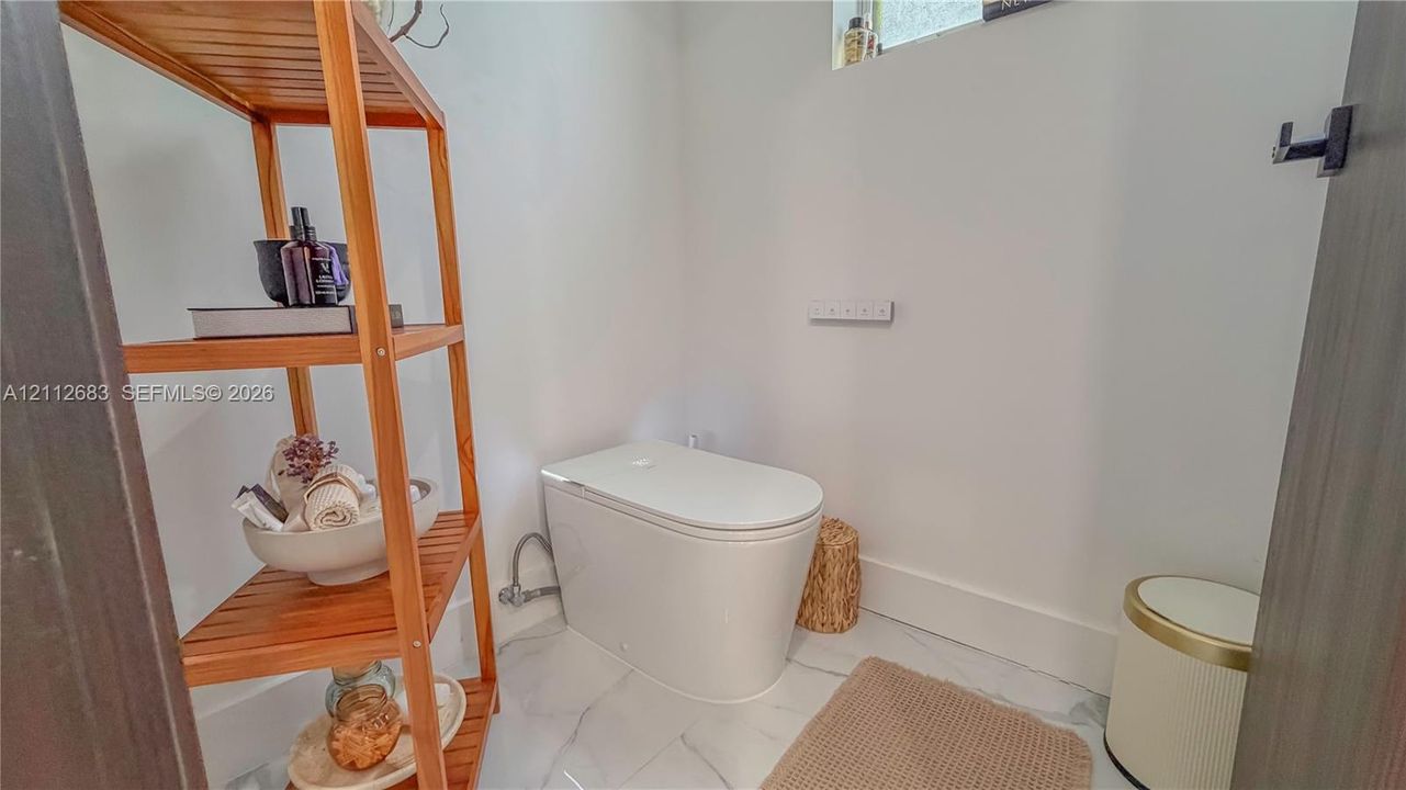 Contemporary one-piece toilet featuring a smooth, minimalist profile and high-gloss white finish, complemented by polished stone-finish flooring with distinct veining