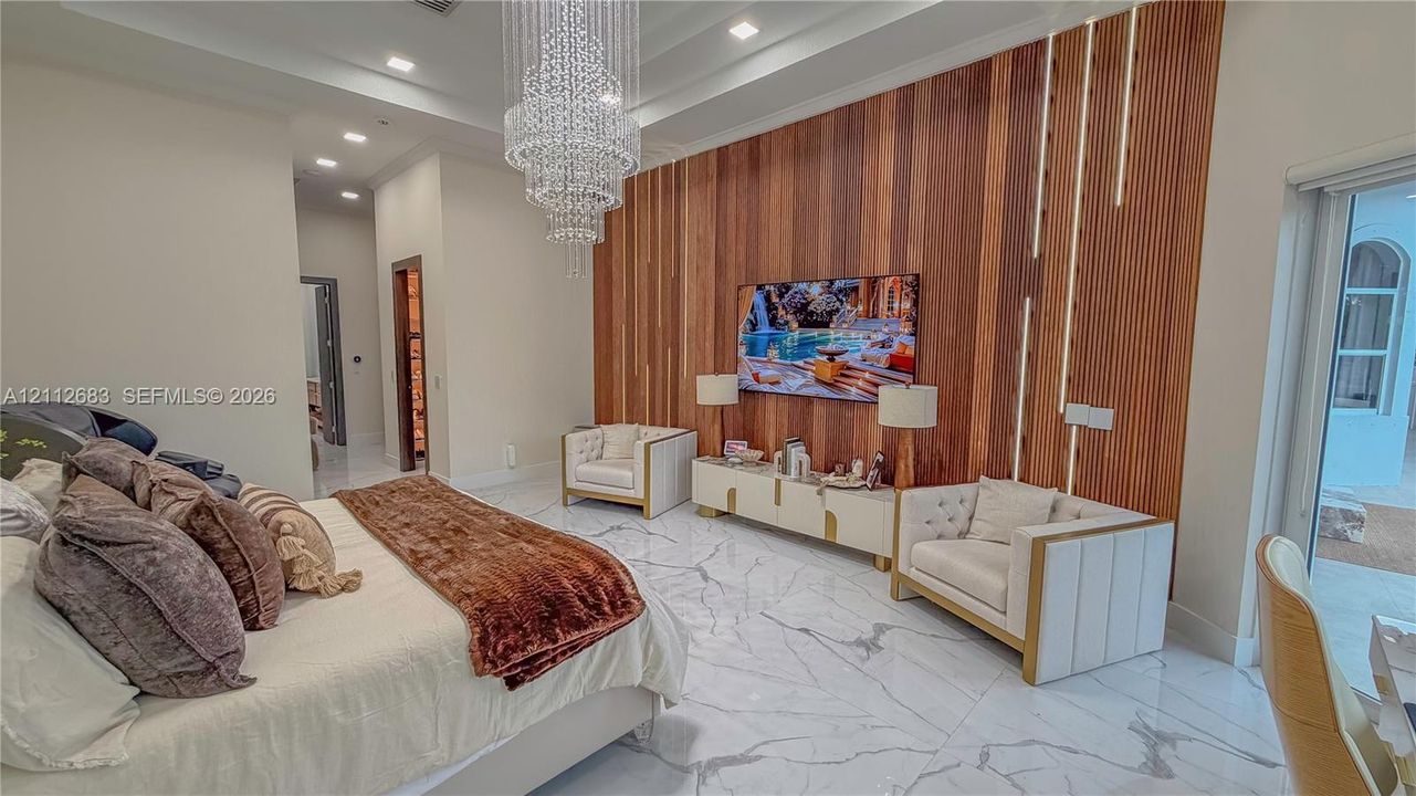 Tray ceiling with recessed lighting, large crystal chandelier, polished stone flooring, and vertical wood-slat accent wall with integrated LED strip lighting