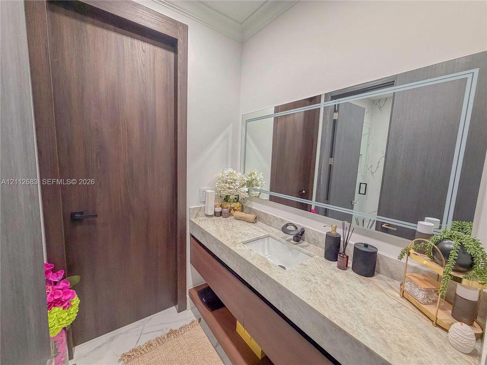 Floating vanity featuring a natural stone countertop, rectangular undermount sink, matte black faucet, and large-format wall mirror with decorative inlay