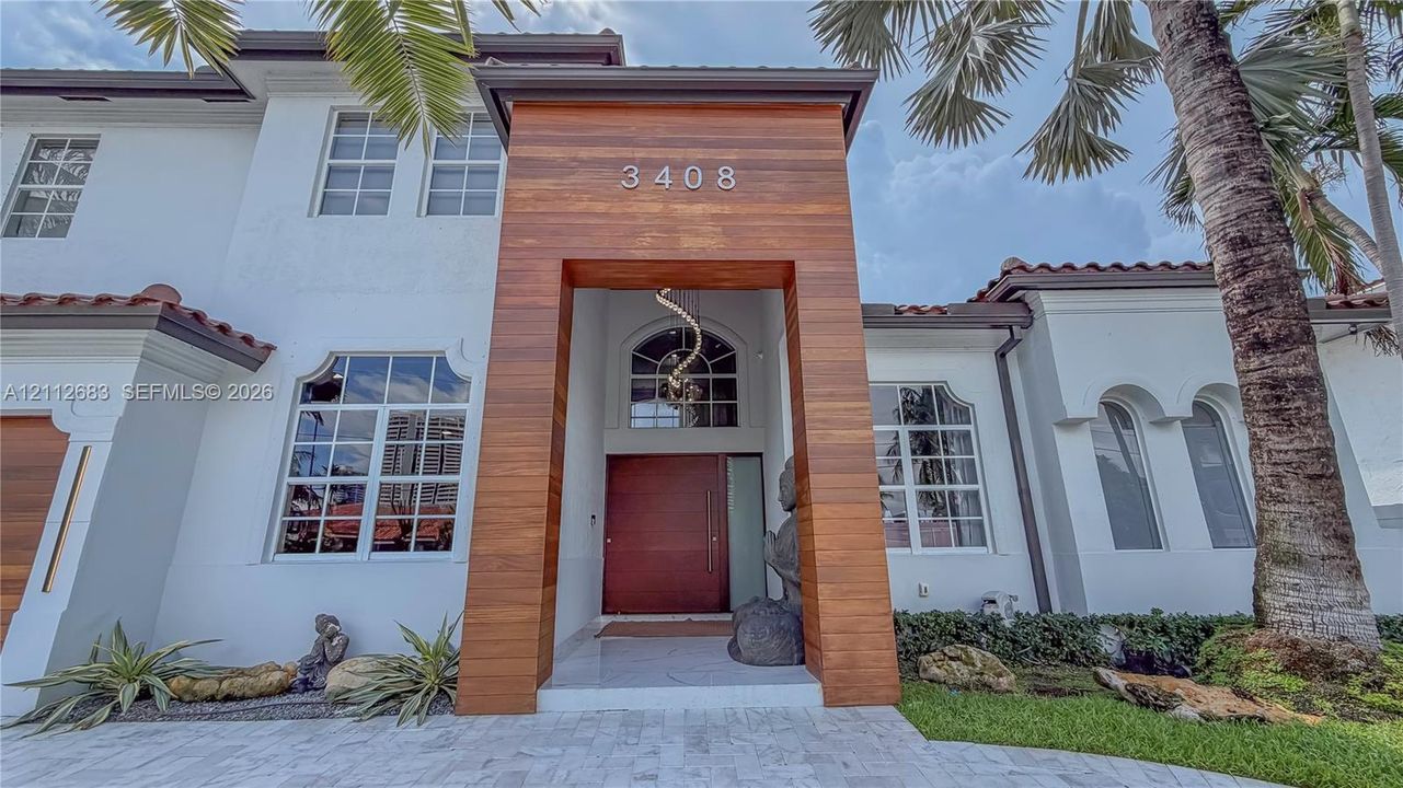 Stucco exterior with a wood-clad entryway, multi-pane arched windows, tile roofing, and stone paver driveway