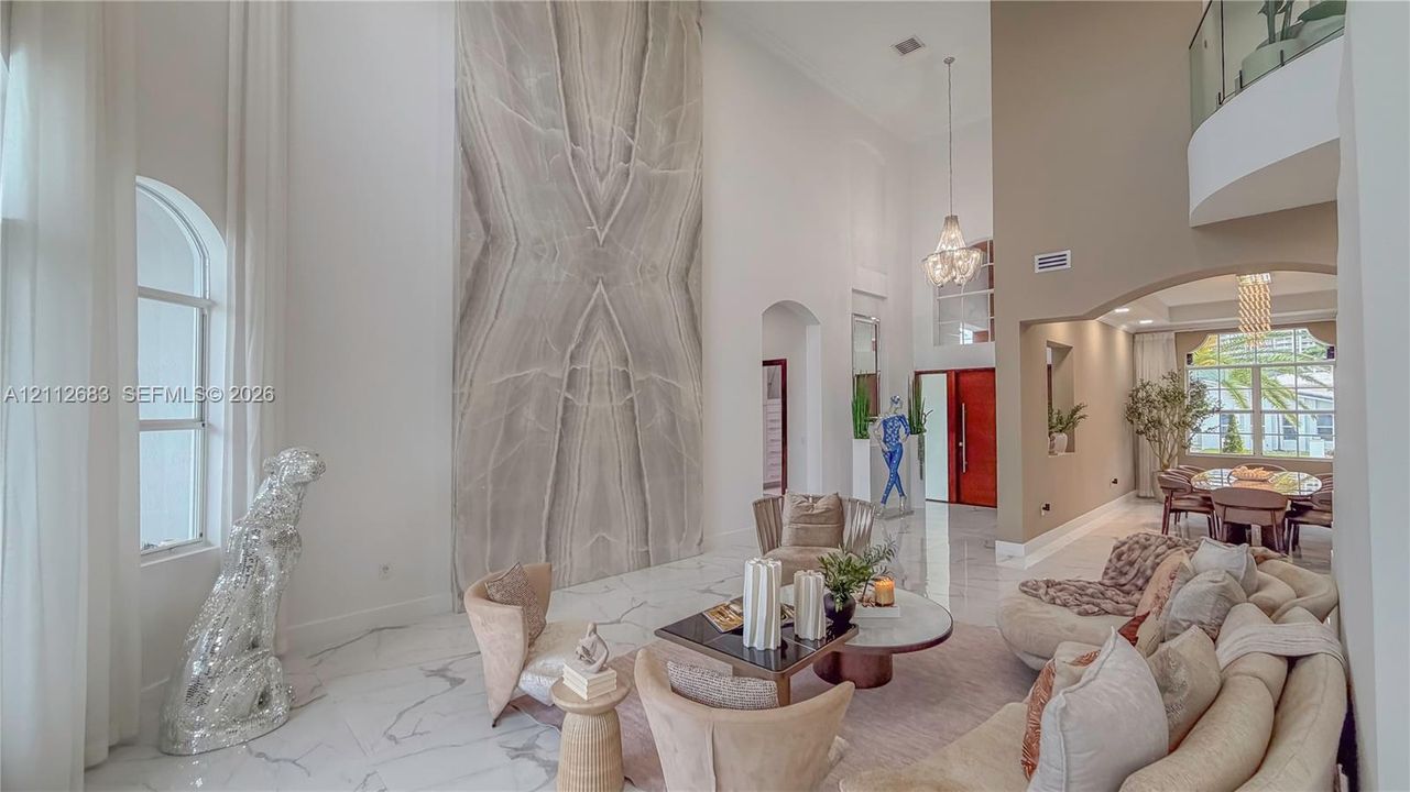 Double-height ceiling, floor-to-ceiling stone-cladding feature wall, polished stone flooring, glass-railing gallery, and tiered crystal chandelier