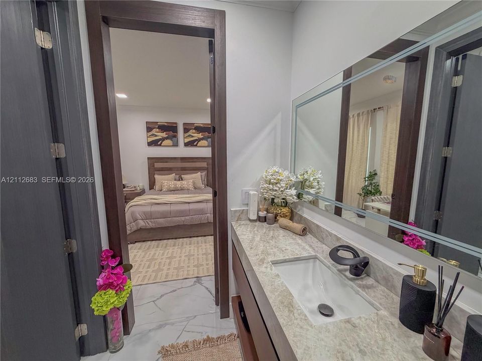Vanity featuring a rectangular undermount sink, stone countertop, matte black faucet, and a large framed mirror with integrated lighting