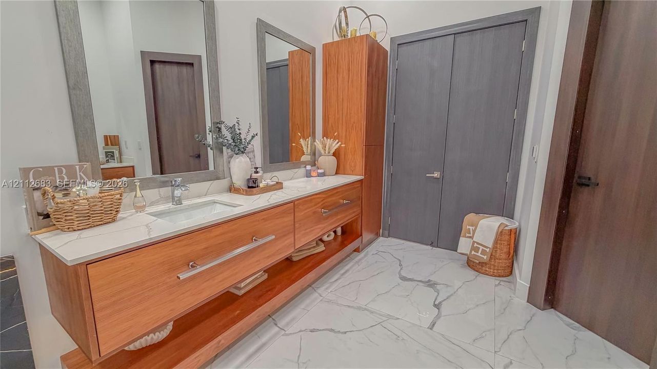 Floating vanity featuring wood-finish cabinetry, a stone-composite countertop with an integrated rectangular sink, dual wall-mounted mirrors with coordinating frames, and large-format porcelain floor tile with veining