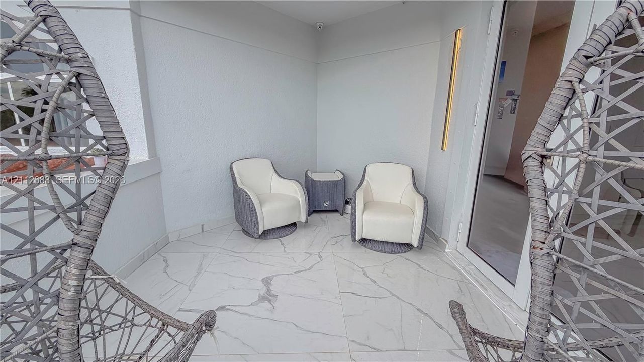 Covered outdoor patio featuring large-format porcelain tile flooring with marble-style veining and a full-height glass entry door