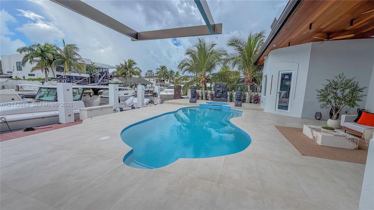 Custom freeform pool featuring built-in steps and light-toned hardscaping, wood-paneled covered patio, and private deep-water dockage