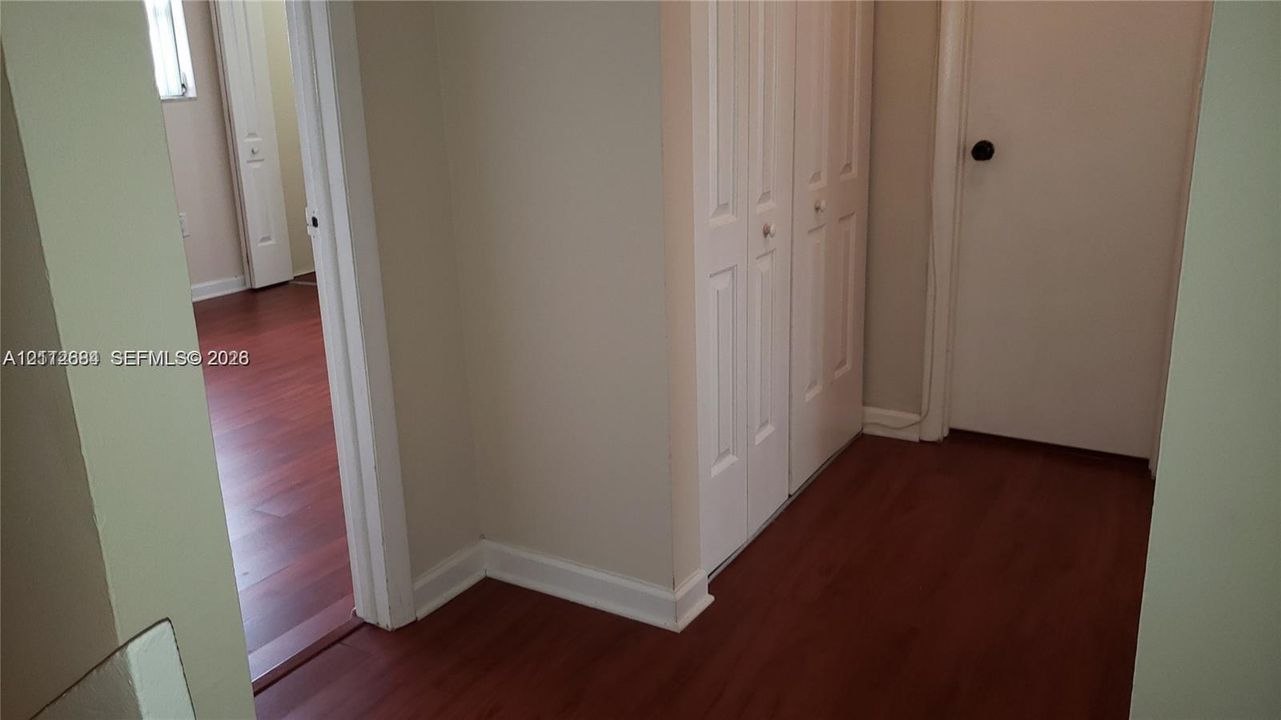 Interior hallway featuring wood-finish flooring, two-panel bifold closet doors, and a solid-core interior door with a matte black handle