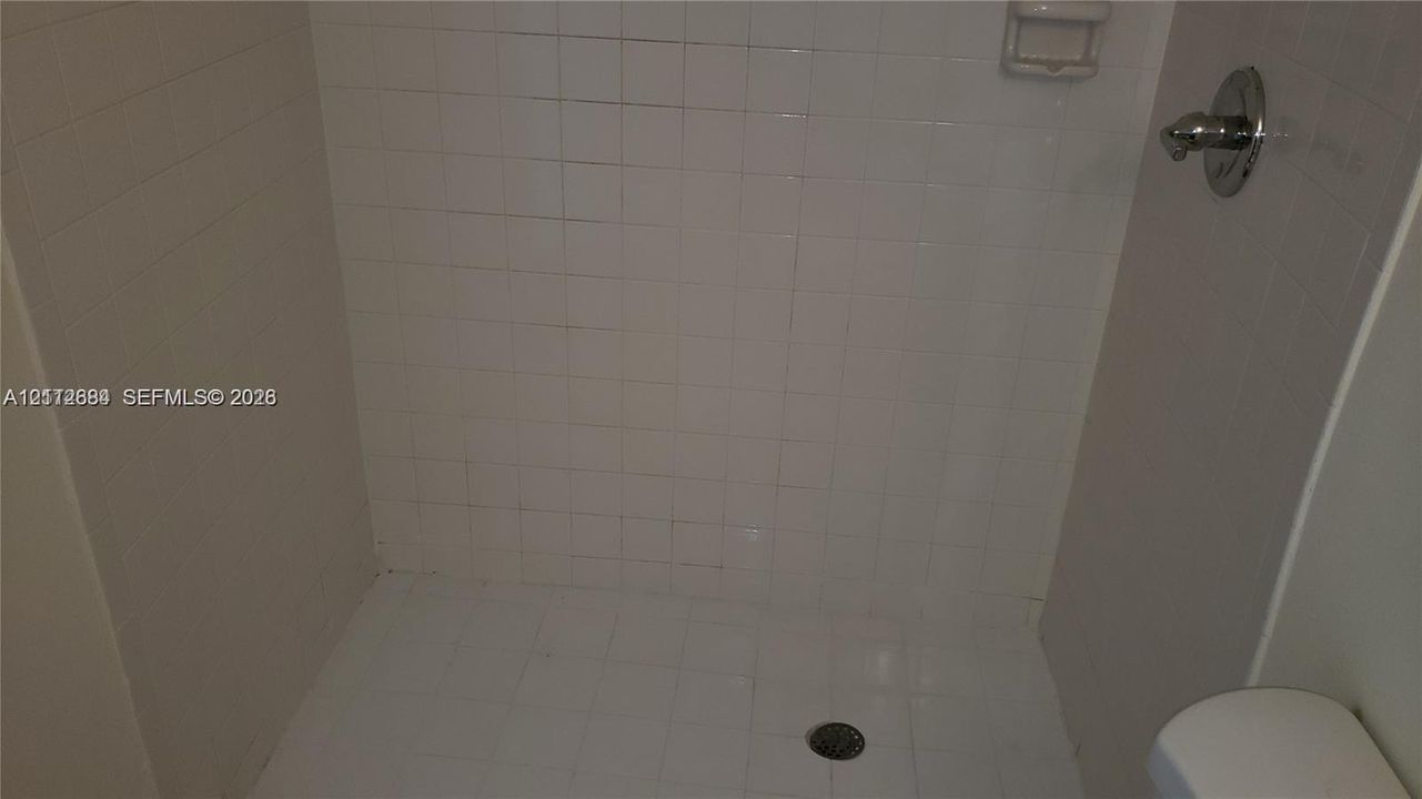 Shower stall featuring white square tile surround, built-in soap niche, and chrome-finish hardware