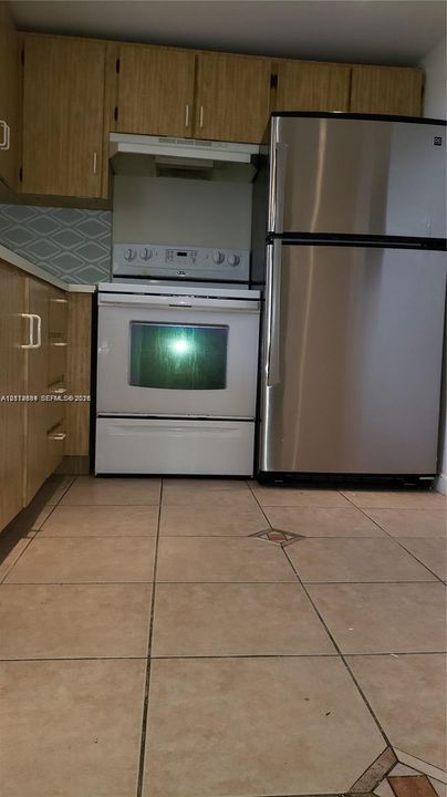 Kitchen featuring wood-finish cabinetry, stainless steel refrigerator, white electric range, and geometric-patterned backsplash tile