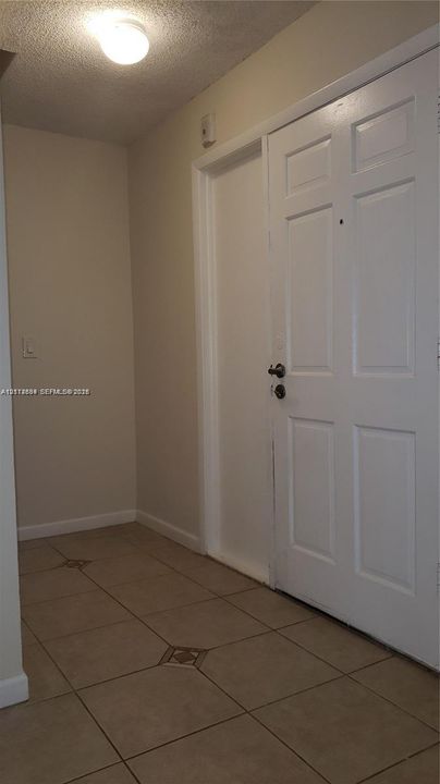 Entryway featuring neutral wall tones, large-format tile flooring with decorative inserts, a six-panel white door, and flush-mount ceiling lighting