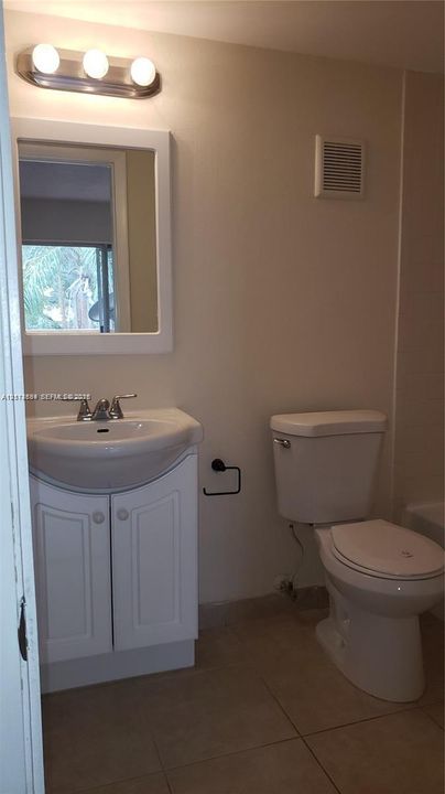 White vanity cabinet with integrated sink, three-light polished chrome fixture, framed wall mirror, and tile flooring
