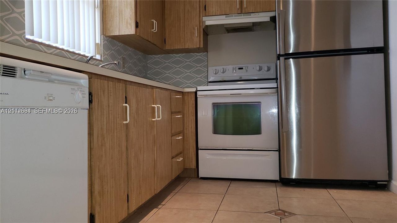 Kitchen featuring wood-finish cabinetry, geometric tile backsplash, tile flooring, and stainless steel refrigerator