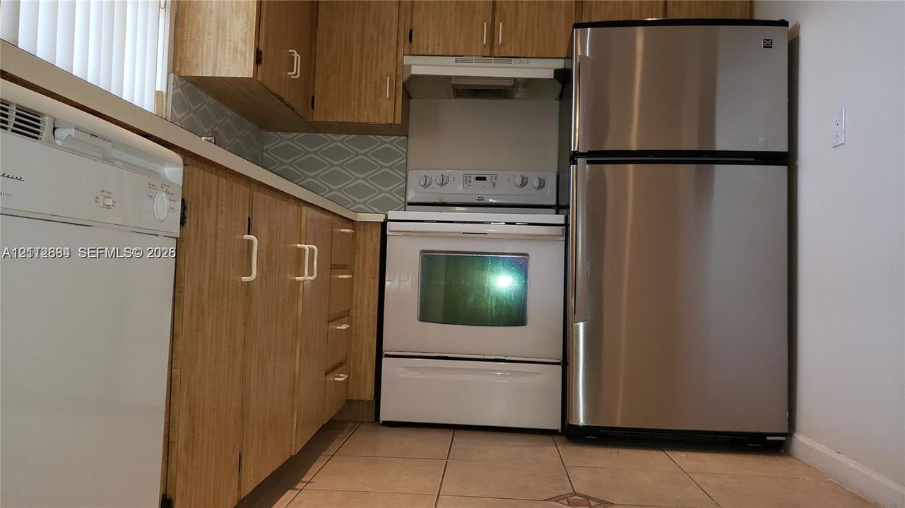 Kitchen featuring wood-finish cabinetry, geometric tile backsplash, stainless steel refrigerator, white range, and tile flooring