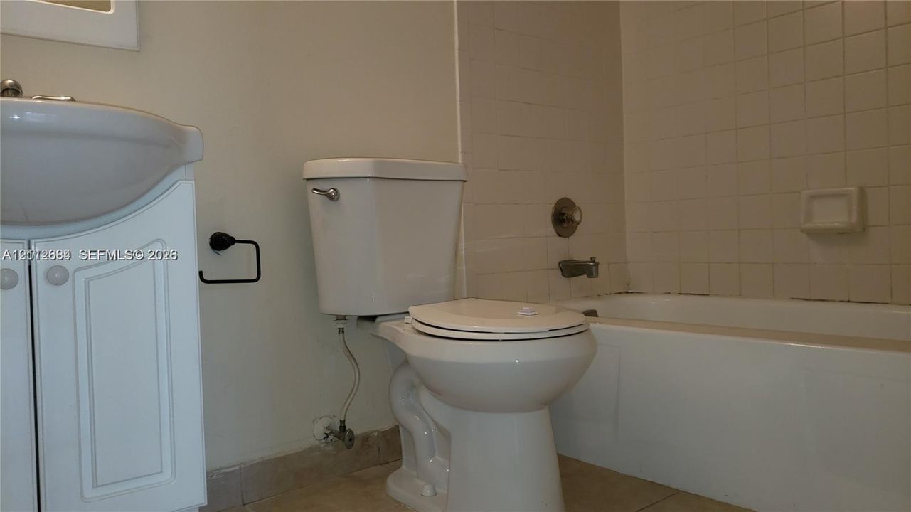 Bathroom featuring a pedestal sink, white toilet, tiled tub surround, and built-in soap dish