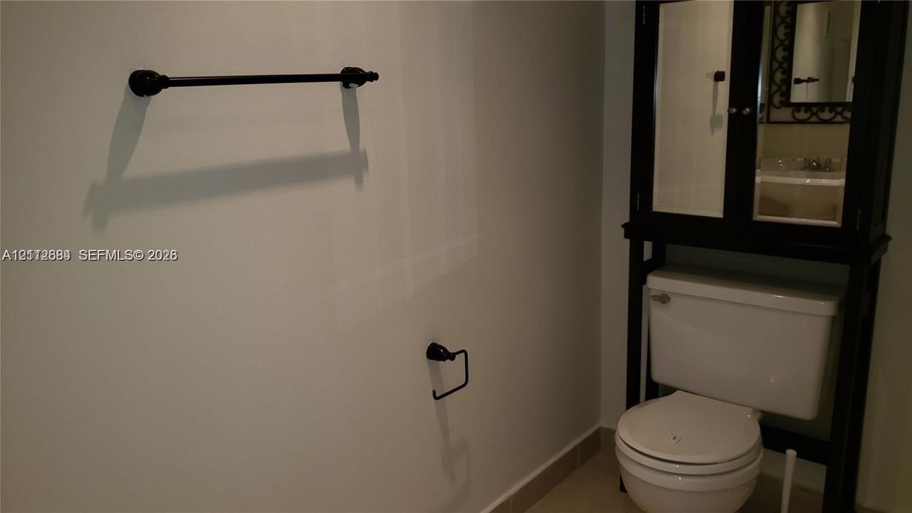 Dark finish over-the-toilet storage unit featuring mirrored doors, wall-mounted matte black towel bar, and coordinating matte black toilet paper holder