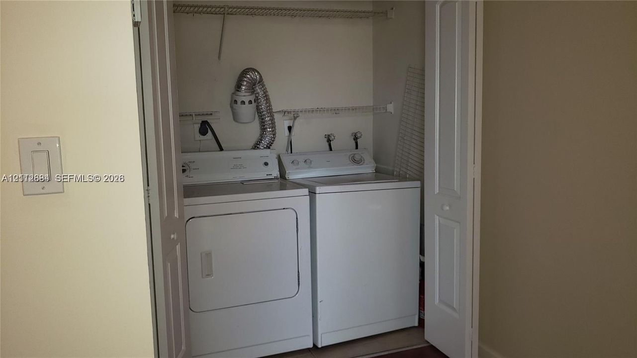 Laundry closet featuring bi-fold doors, white top-load washer, white dryer, and built-in wire shelving