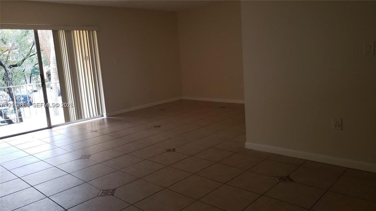 Neutral-toned interior space featuring light-colored square tile flooring with decorative tile inlays and glass sliding doors leading to an exterior balcony
