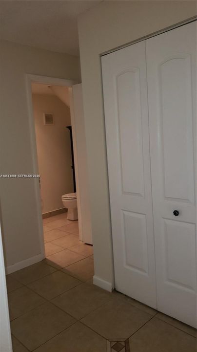 Neutral-toned interior featuring ceramic tile flooring and a double-door closet with recessed paneling and matte black hardware