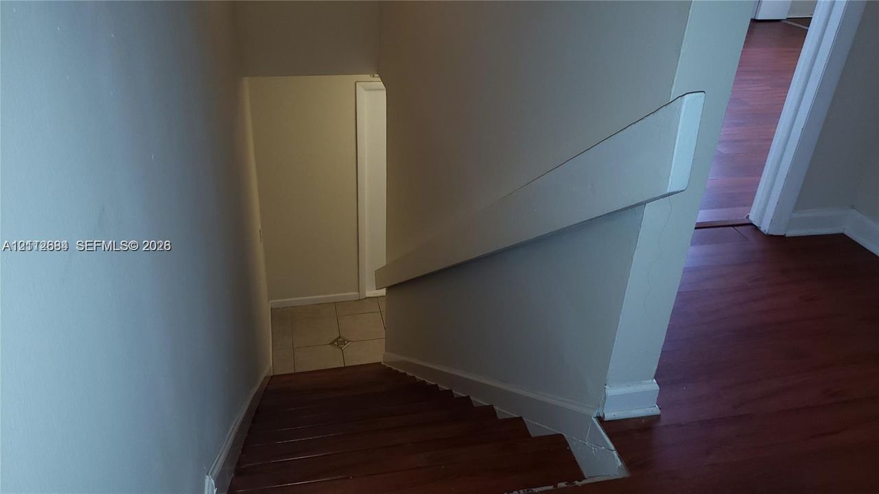 Staircase featuring wood-finish treads and a painted wall-mounted handrail