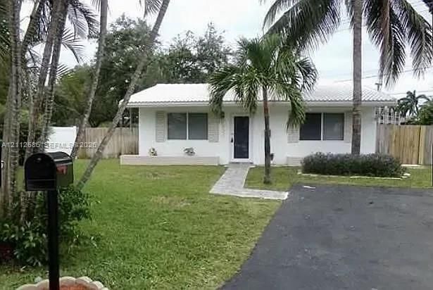 Single-story exterior featuring white stucco siding, a light-toned tile roof, a paved walkway, an asphalt driveway, and mature palm trees
