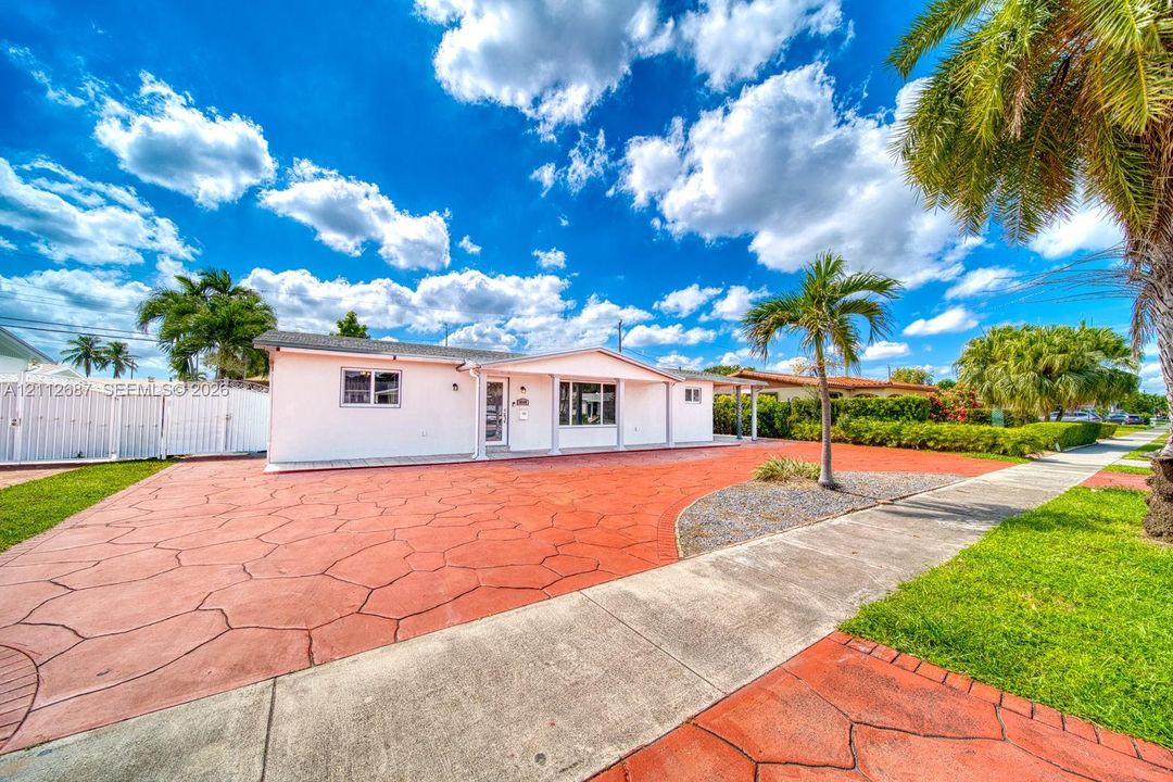 Single-story exterior featuring white stucco siding, expansive stamped concrete driveway, and mature landscaping