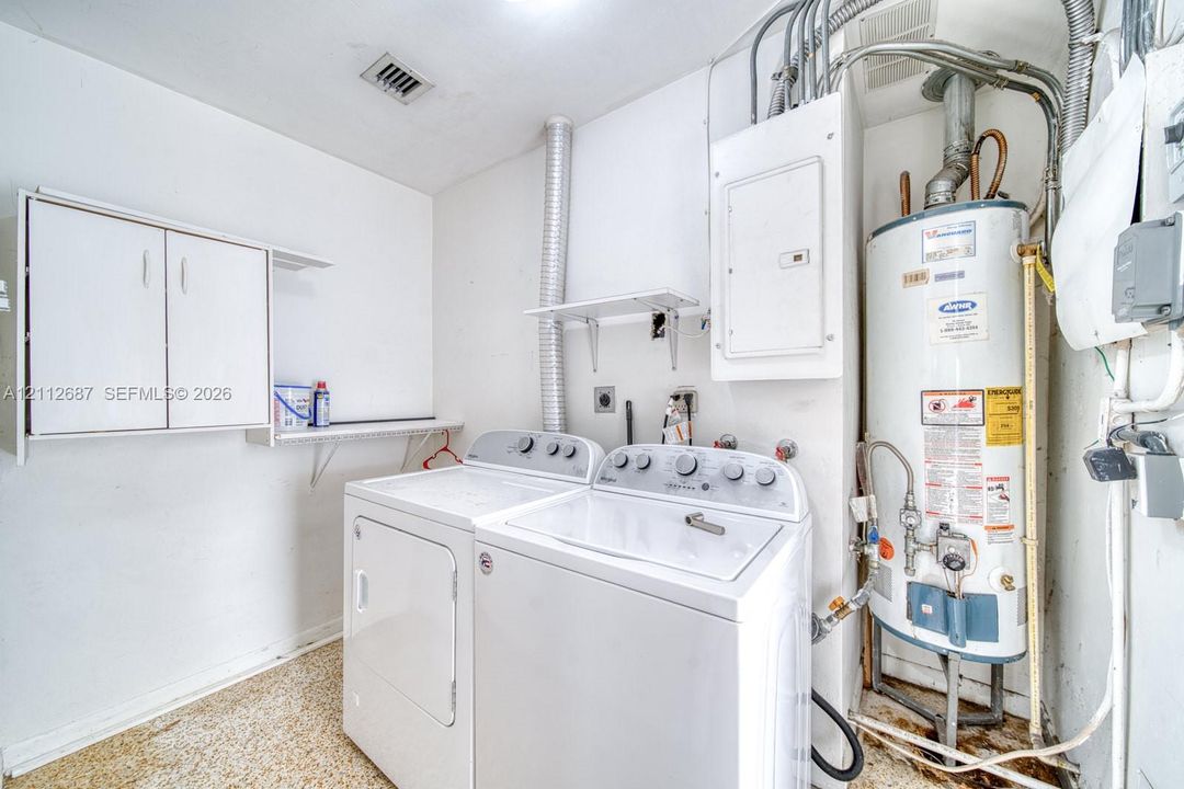 Utility area featuring white wall-mounted cabinetry, integrated open shelving, and a dedicated tank-style water heater