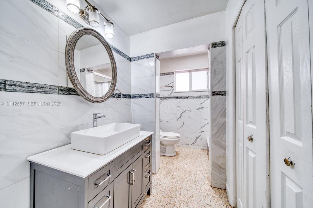 Bathroom featuring a floating vanity with a rectangular vessel sink, polished chrome faucet, wall-mounted oval mirror, and full-height stone-finish wall tile with decorative accent inlay