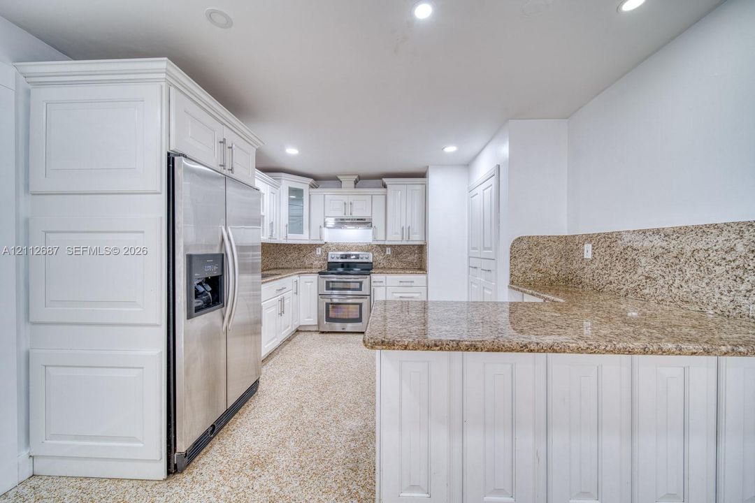Kitchen featuring custom white cabinetry, stone countertops with matching backsplash, stainless steel appliances, and recessed lighting