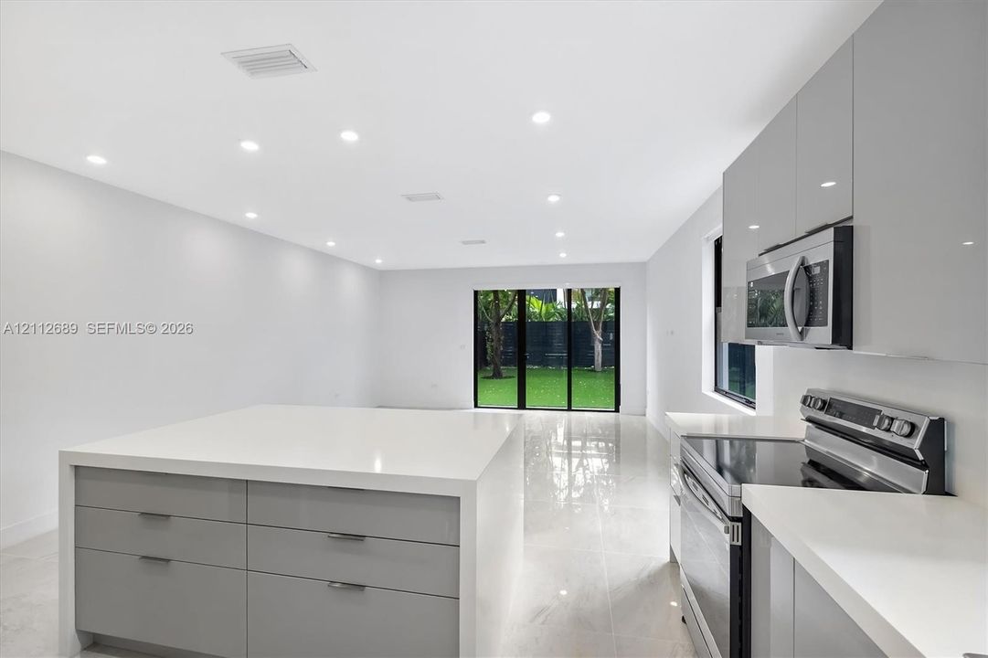 Modern kitchen featuring high-gloss cabinetry, stone-surface waterfall island, stainless steel appliances, recessed ceiling lighting, and polished tile flooring